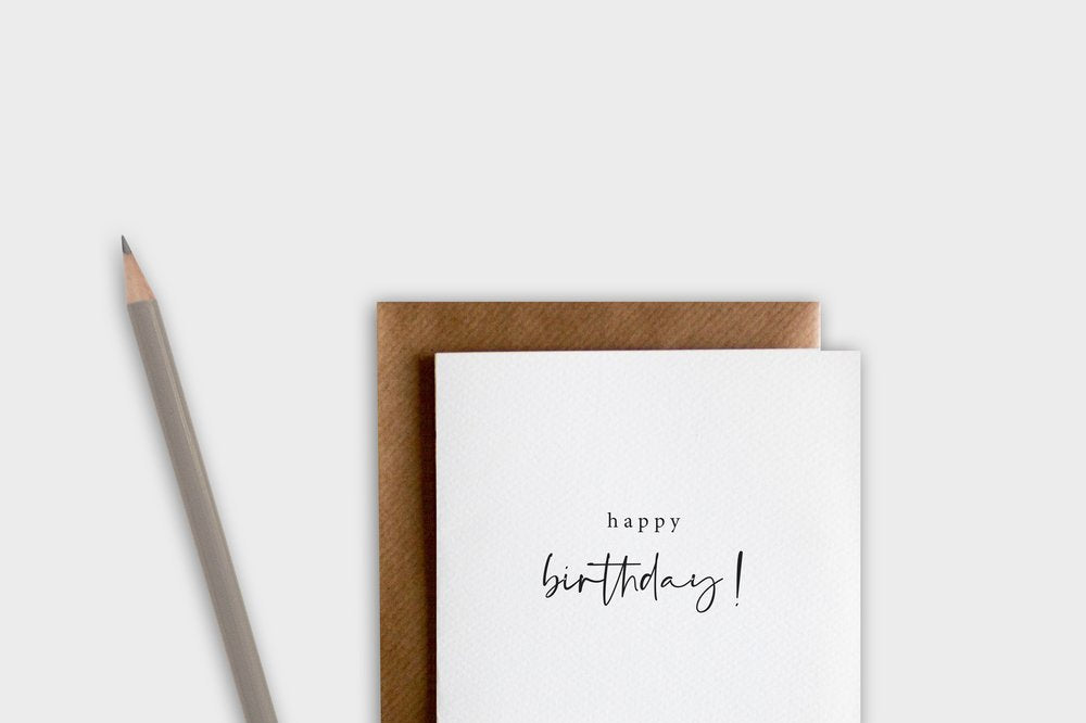 White card with 'happy birthday!' text, brown envelope, and pencil on a white background