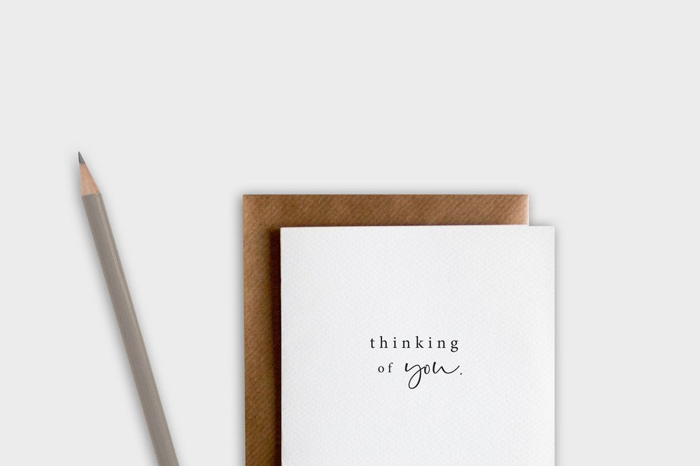Greeting card with 'thinking of you' text, brown envelope, and pencil on a white background