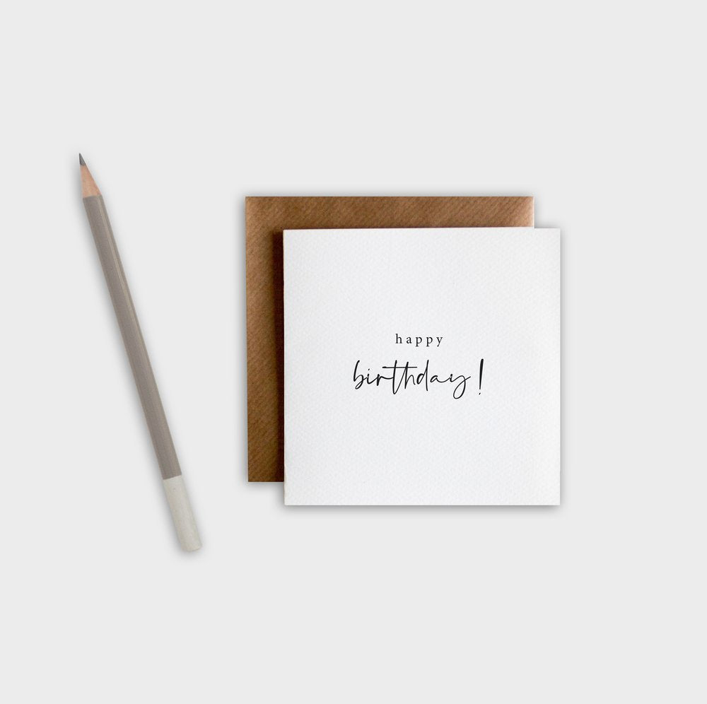 White card with 'happy birthday!' text, brown envelope, and pencil on a white background