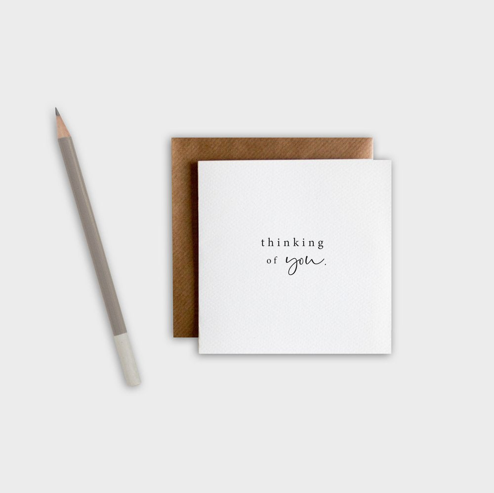 Greeting card with 'thinking of you' text, brown envelope, and pencil on a white background